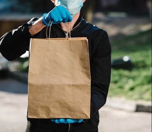 Delivery driver wearing gloves and a mask while holding a bag of food.