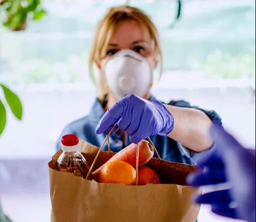 A woman wearing mask and gloves holding a bag of groceries.
